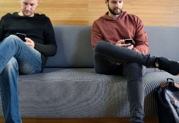 two men sitting on couch looking at phones